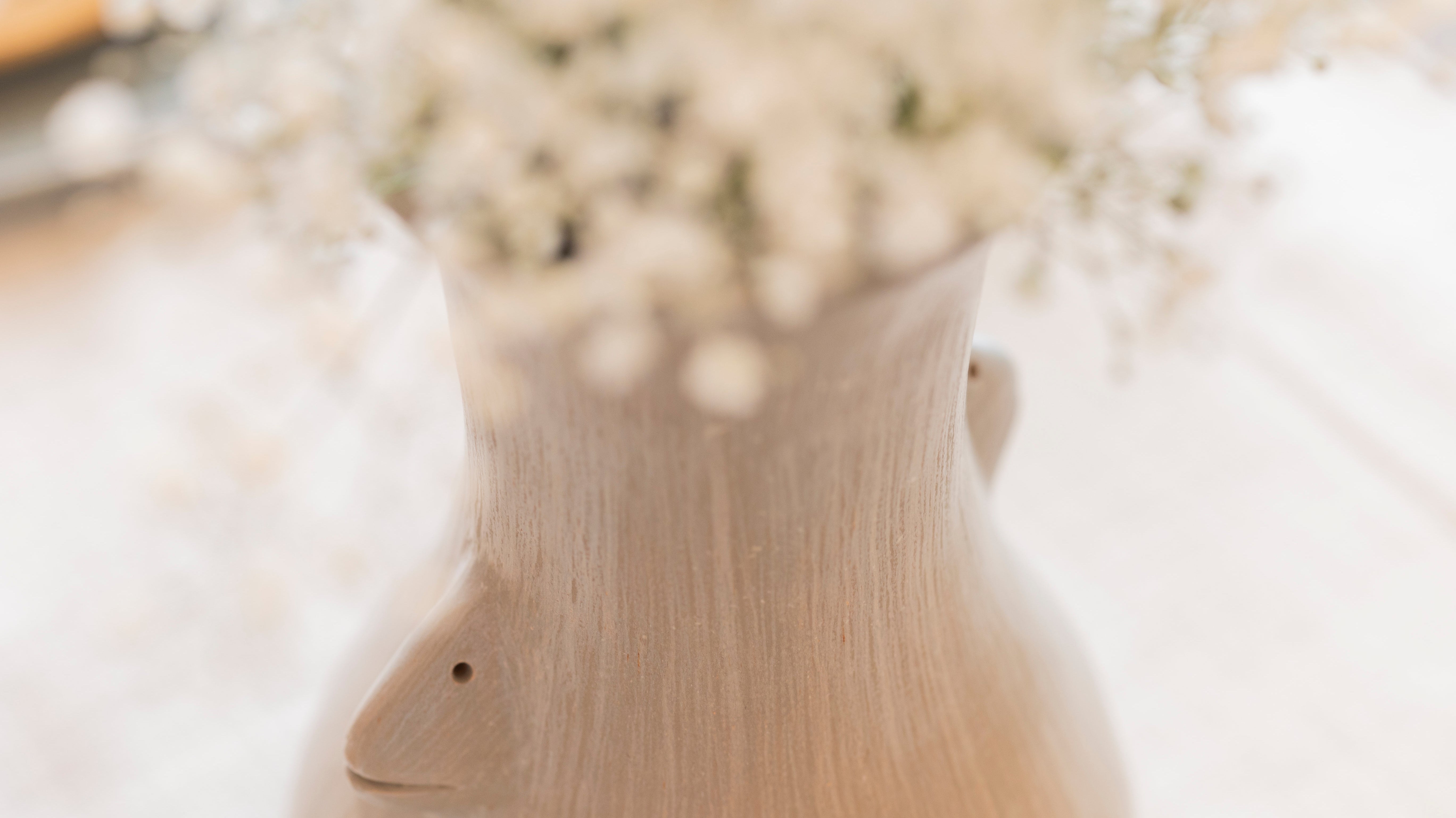 Close-up of a handcrafted ceramic vase with sculpted face detail, holding delicate white baby’s breath flowers on a linen-covered table.