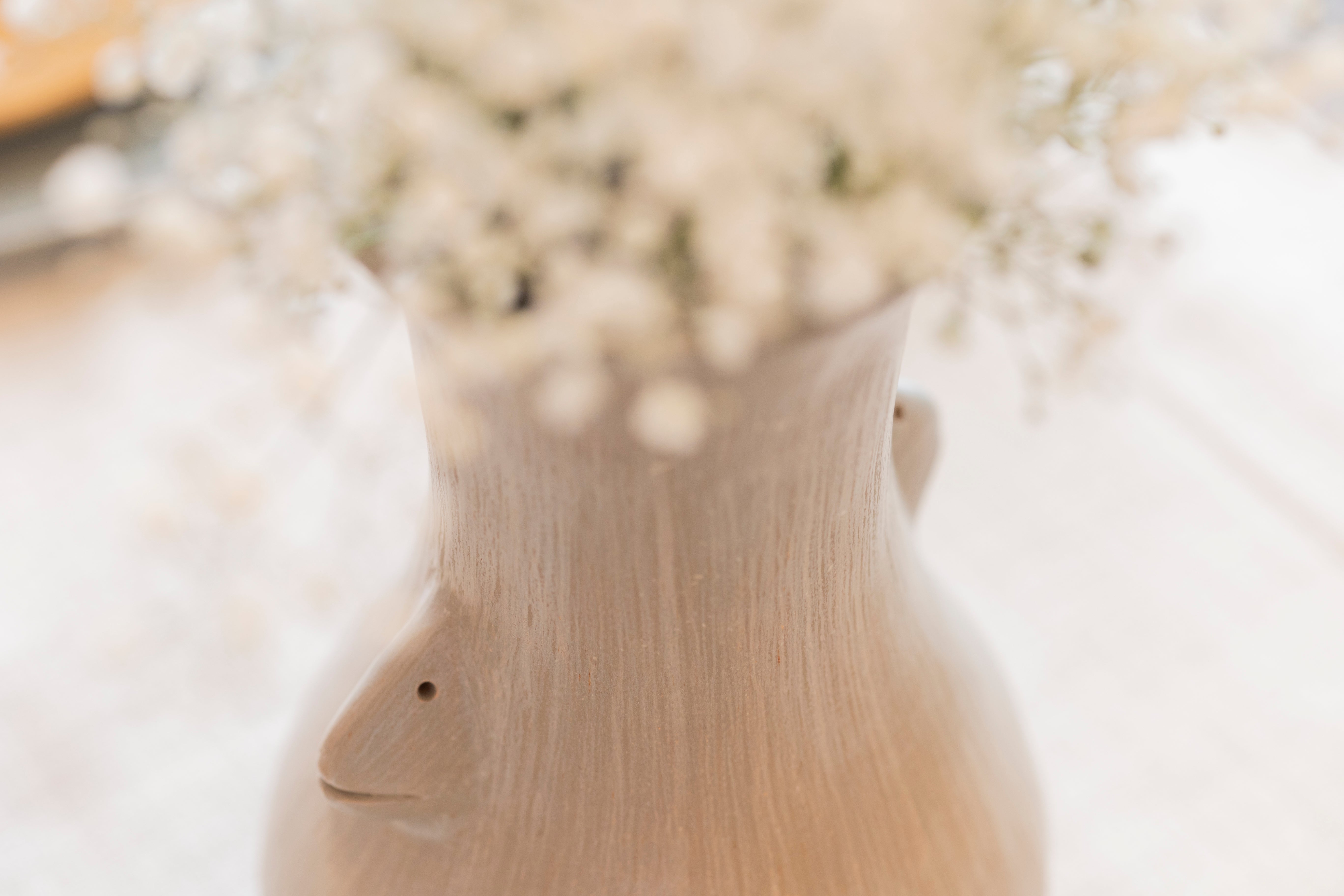 Close-up of a handcrafted ceramic vase with sculpted face detail, holding delicate white baby’s breath flowers on a linen-covered table.